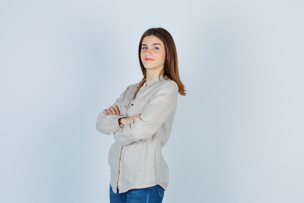 Young girl in beige shirt, jeans standing arms crossed and looking confident , front view.