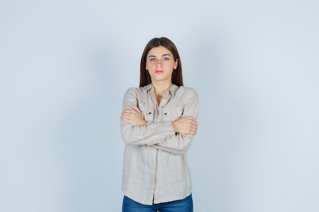 Free photo young girl in beige shirt, jeans standing arms crossed and looking serious , front view.