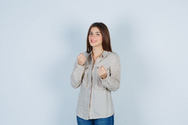 Young girl in beige shirt, jeans standing in fight pose and looking confident , front view.