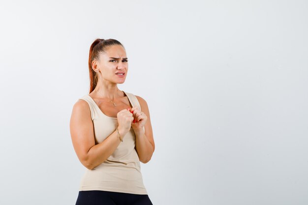 Young girl in beige top, black pants holding clenched fists over chest and looking scared , front view.