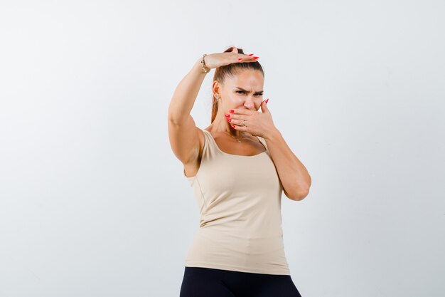 Young girl in beige top, black pants holding hand above head, covering mouth with hand