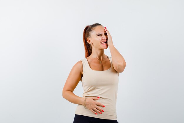 Young girl in beige top, black pants holding one hand on head, another hand on belly