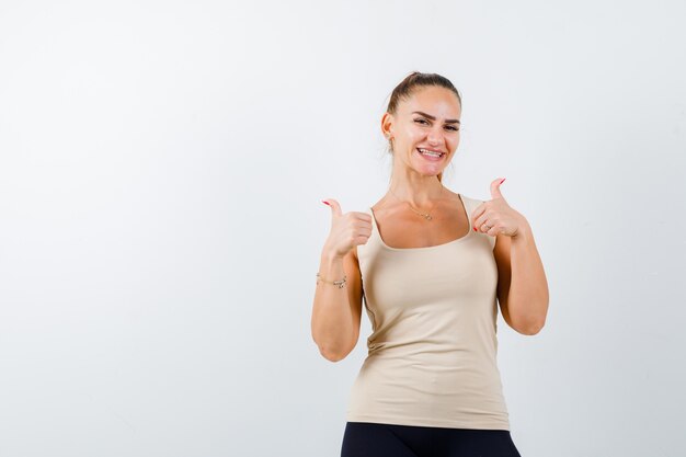 Young girl in beige top, black pants showing double thumbs up and looking cheery , front view.