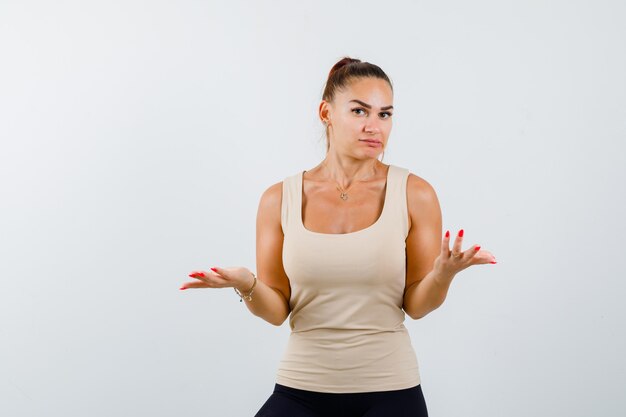 Free photo young girl in beige top, black pants showing helpless gesture and looking baffled