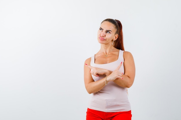 Young girl in beige top and red pants pointing opposite directions with index fingers