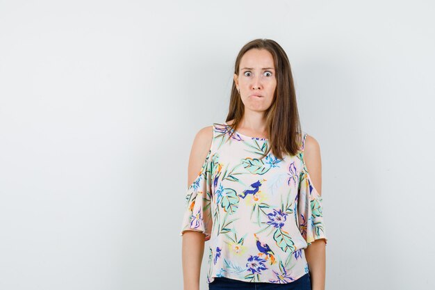 Young girl biting lip in shirt, jeans and looking anxious , front view.