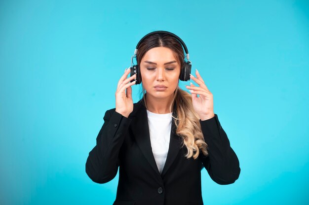 Young girl in black blazer wearing headphones and relaxing.