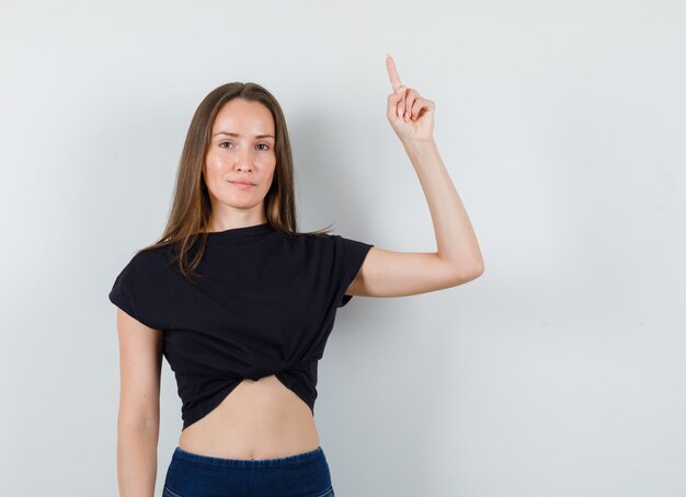 Young girl in black blouse, pants pointing up and looking glad