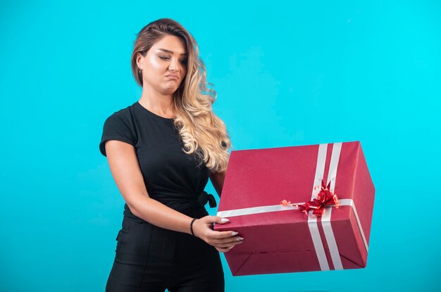 Young girl in black shirt holding a big gift box and looks confused.