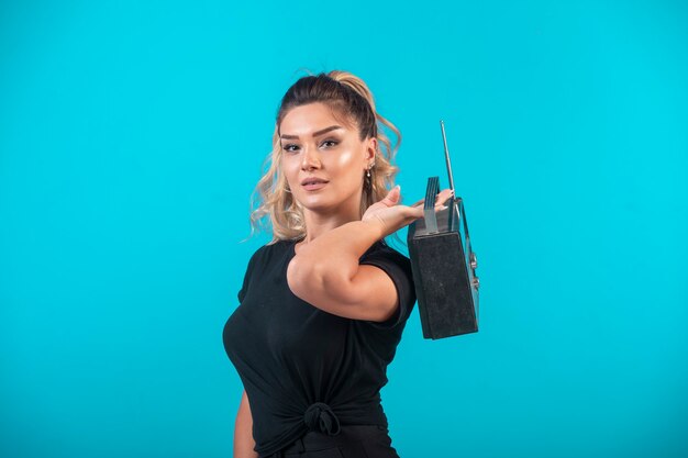 Young girl in black shirt holding a vintage radio on her back.