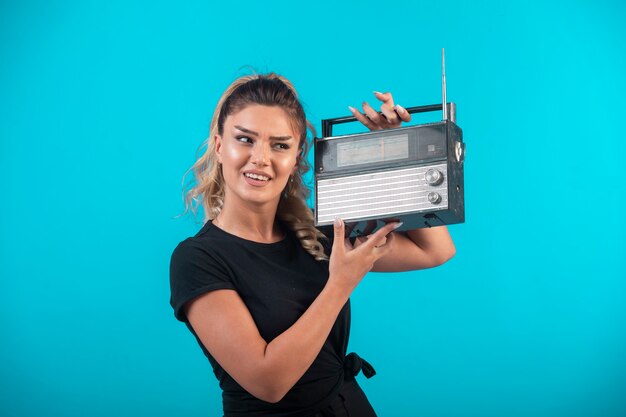 Young girl in black shirt holding a vintage radio on her shoulder and feels positive. 