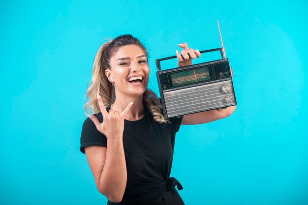 Young girl in black shirt holding a vintage radio on her shoulder and feels positive.