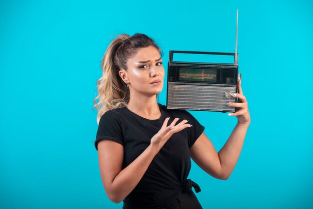 Young girl in black shirt holding a vintage radio on her shoulder.