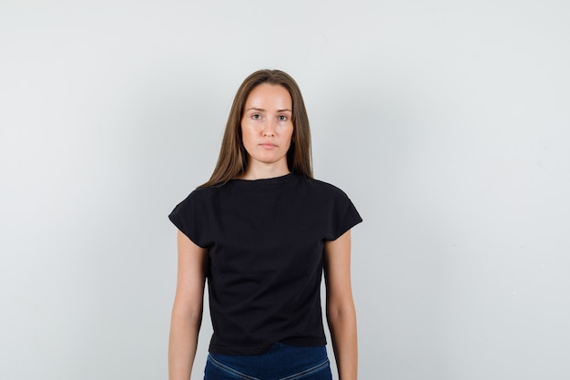 Free photo young girl in black t-shirt, pants looking at camera and looking serious