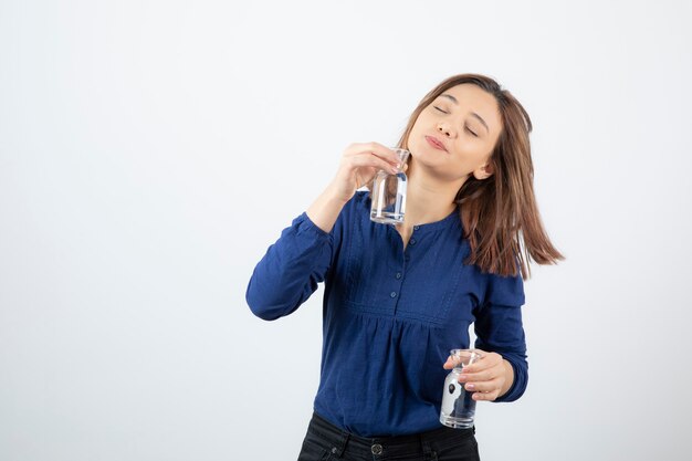 young girl in blue blouse trying to drink glass of water.