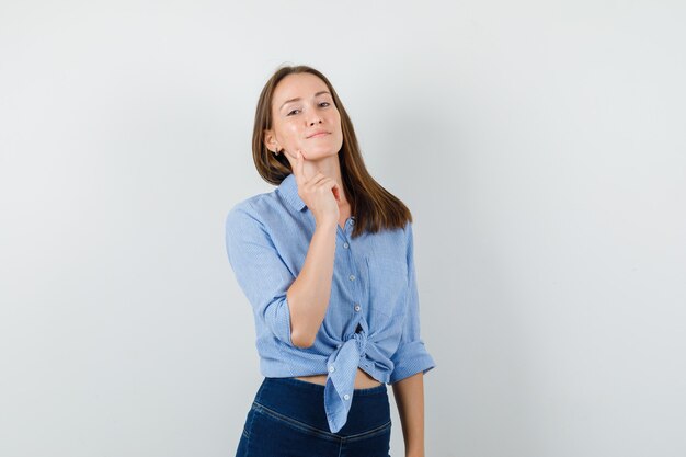 Young girl in blue shirt, pants holding finger on chin and looking confident