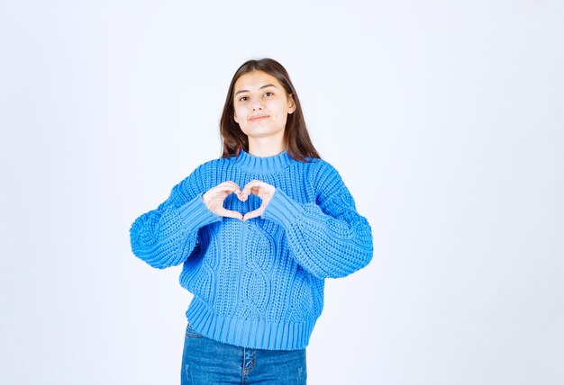 молодая девушка в синем свитере показывает сердце двумя руками.