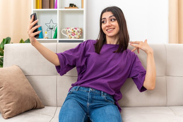 Young girl in casual clothes doing selfie using smartphone smiling confident sitting on a couch in light living room