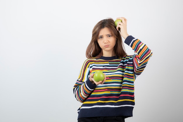 Young girl in casual clothes standing with green apples on white.