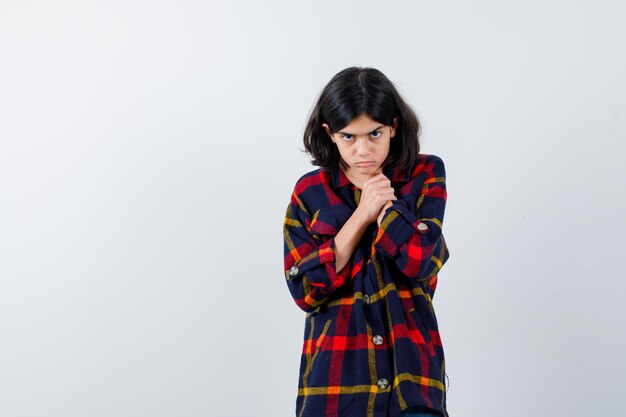 Young girl in checked shirt holding hands on neck and looking exhausted , front view.