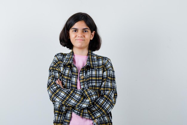 Young girl in checked shirt and pink t-shirt standing arms crossed and looking happy