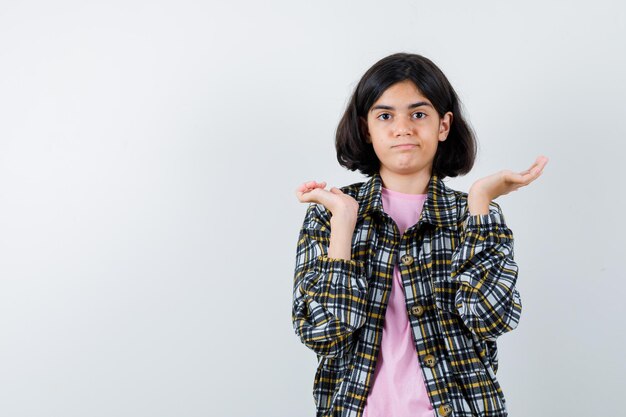 Young girl in checked shirt and pink t-shirt stretching hands in questioning manner and looking baffled