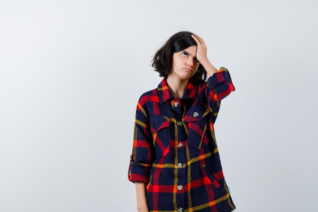 Young girl in checked shirt putting hand on head and looking annoyed , front view.