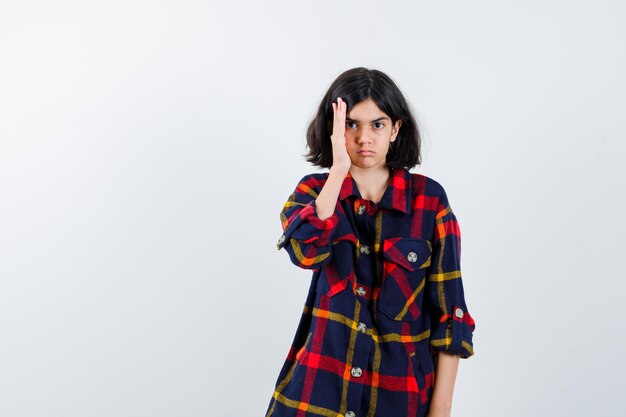 Free photo young girl in checked shirt putting hand near face and looking serious , front view.