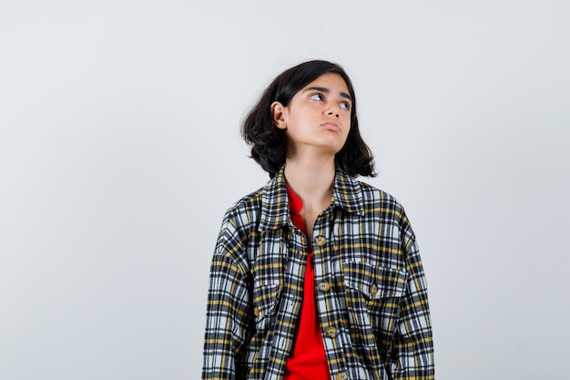 Giovane ragazza in camicia a quadri e t-shirt rossa che distoglie lo sguardo mentre posa alla macchina fotografica e sembra seria, vista frontale.