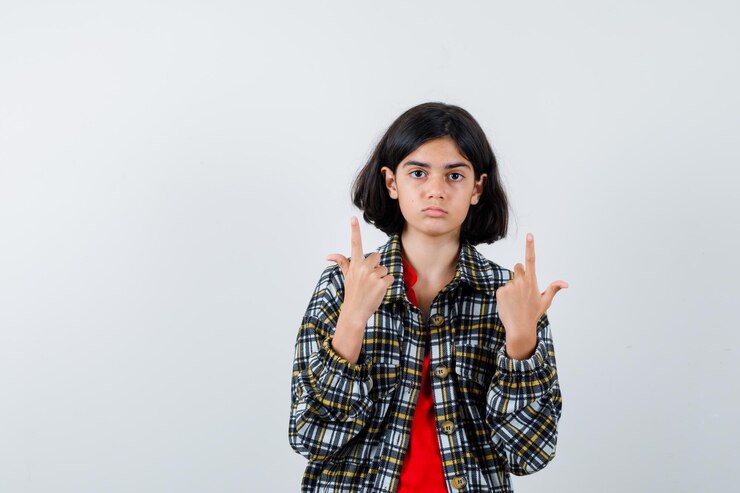 मुफ़्त फोटो young girl in checked shirt and red t-shirt pointing up and looking cute , front view.