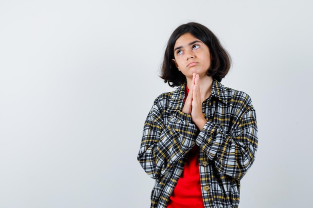 Young girl in checked shirt and red t-shirt praying and looking serious , front view.