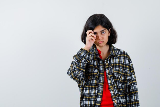 Young girl in checked shirt and red t-shirt scratching face and looking serious , front view.