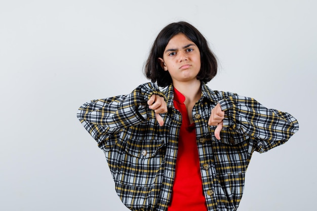 Free photo young girl in checked shirt and red t-shirt showing thumbs down with both hands and looking displeased , front view.