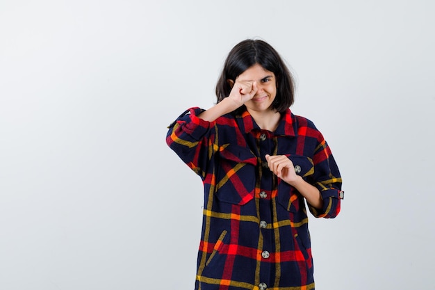 Young girl in checked shirt rubbing eye and looking tired , front view.