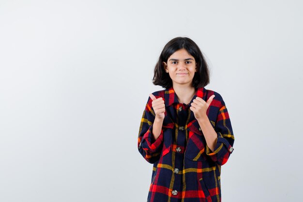 Young girl in checked shirt showing thumbs down with both hands and looking happy , front view.