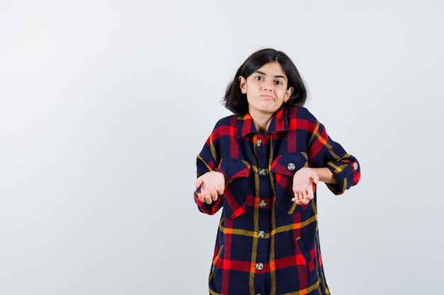 Young girl in checked shirt stretching hands in questioning manner and looking puzzled , front view.