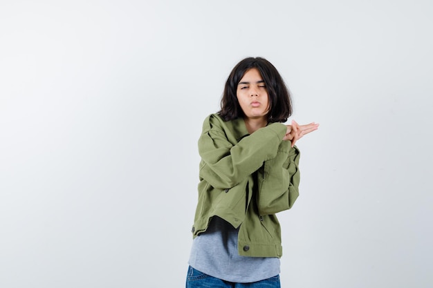 Young girl clasping hands, closing eyes in grey sweater, khaki jacket, jean pant and looking tired , front view.