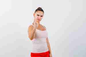 Free photo young girl clenching fist in beige top and red pants and looking confident. front view.