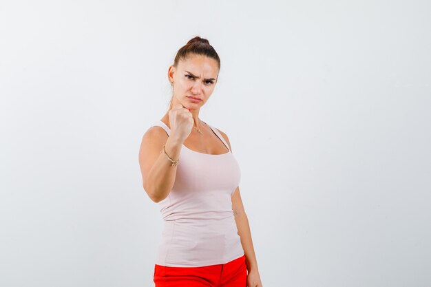 Young girl clenching fist in beige top and red pants and looking confident. front view.