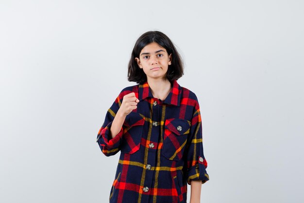 Young girl clenching fist in checked shirt and looking cute , front view.