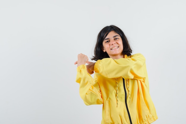 어린 소녀 주먹 떨림과 노란색 폭격기 재킷에 왼쪽을 가리키는 행복 찾고.