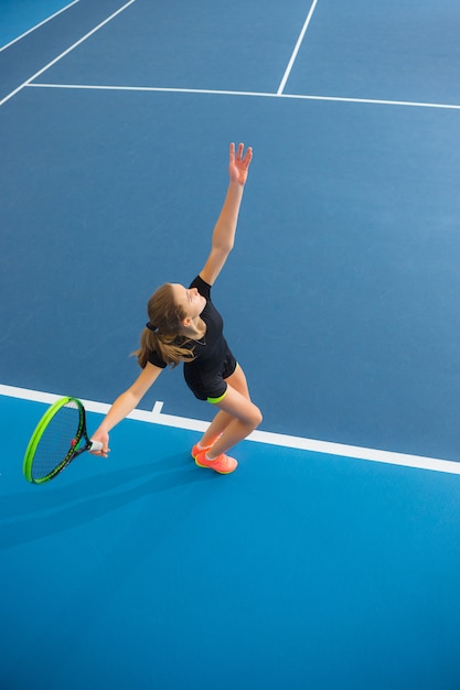 The young girl in a closed tennis court with ball