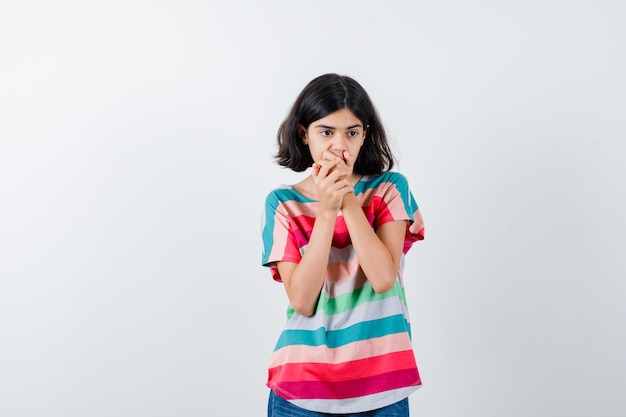 Free photo young girl in colorful striped t-shirt covering mouth with hands and looking surprised , front view.