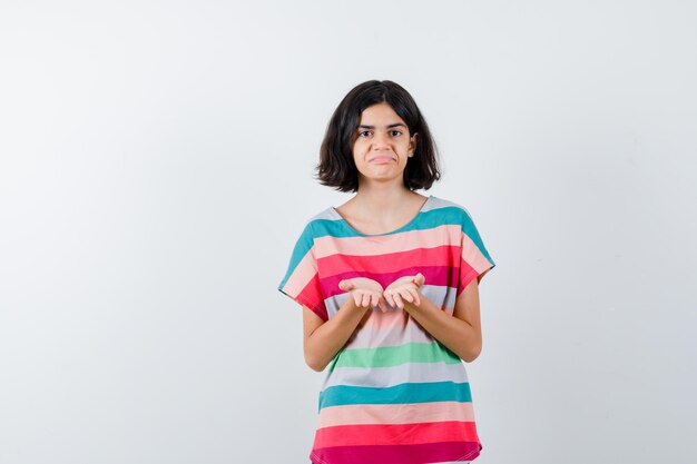 Young girl in colorful striped t-shirt inviting to come and looking happy , front view.