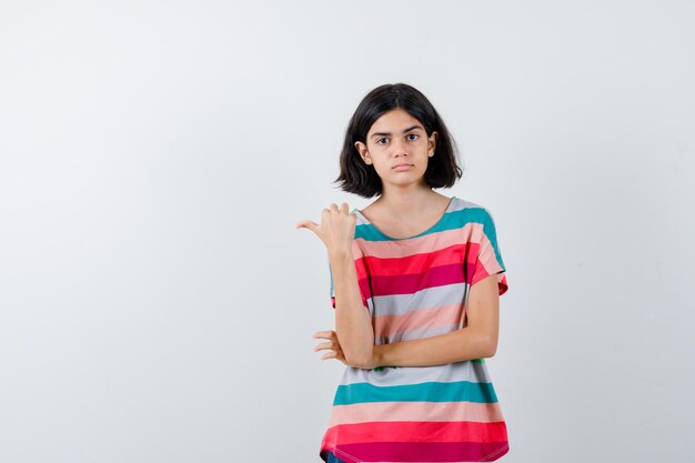 Молодая девушка в красочной полосатой футболке, указывая влево и серьезно, вид спереди.