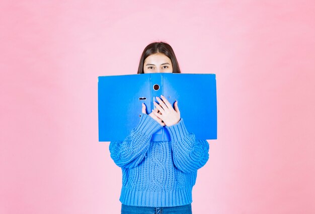 Foto gratuita giovane ragazza coning viso con una cartella blu su rosa.