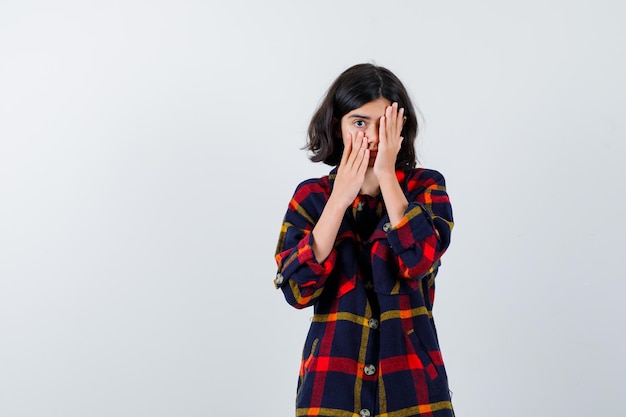 Young girl covering eye with hand in checked shirt and looking serious. front view.