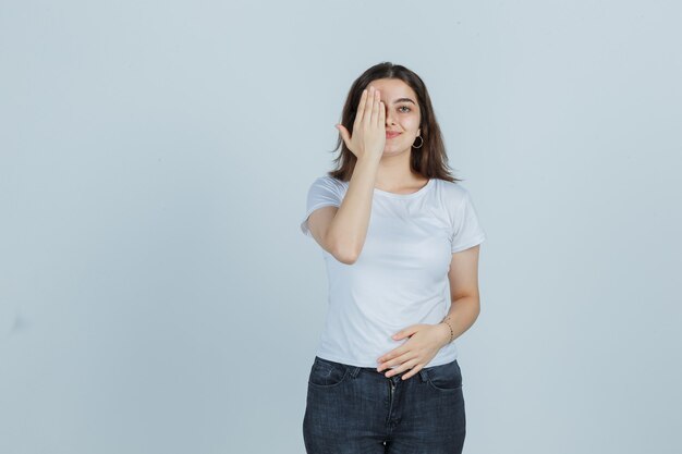 Tシャツ、ジーンズ、幸せそうに見える、正面図で手で目を覆っている少女。