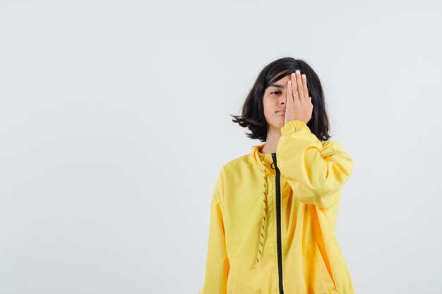 노란색 폭격기 재킷에 한 손으로 눈을 덮고 심각한 찾고 어린 소녀.