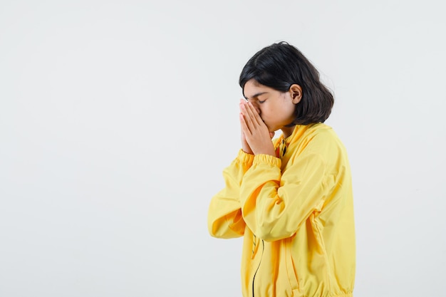 Young girl covering eye with one hand in yellow bomber jacket and looking serious.